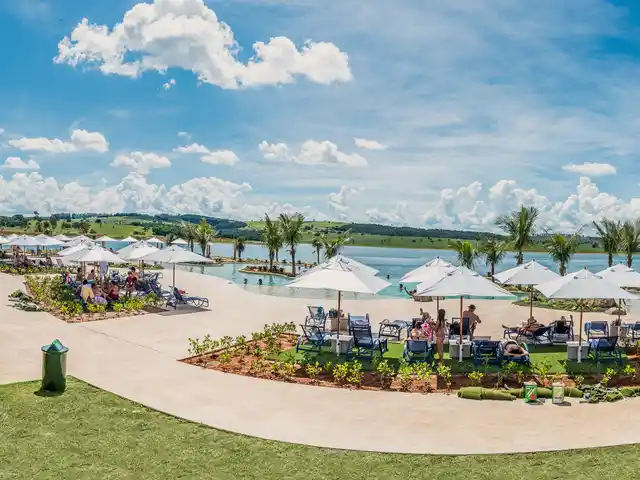 Praia de água doce com ombrelones, o gramado e a represa ao fundo.